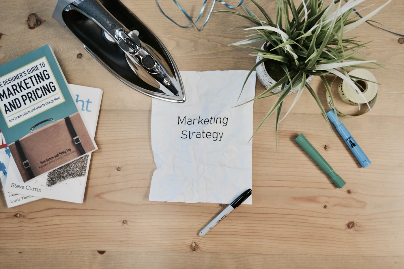 Desk with a handwritten marketing strategy note, pens and a plant