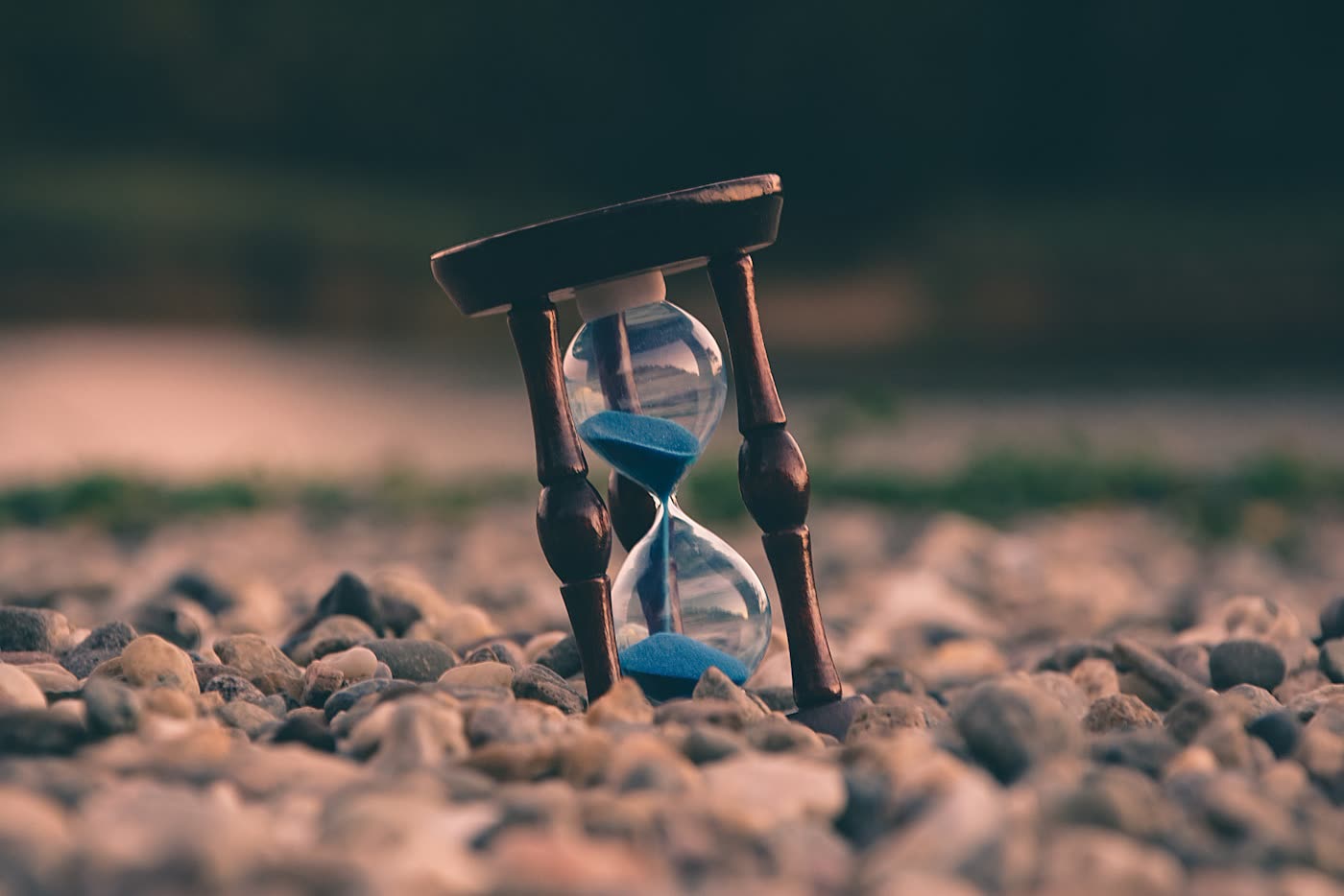 Hourglass with blue sand standing on pebbles — watch time running