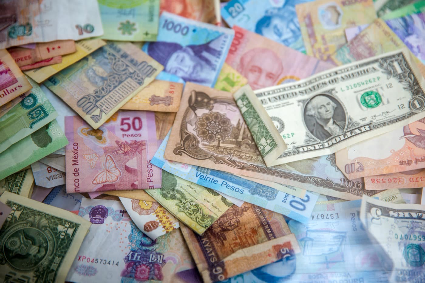 Banknotes from many world currencies spread across a table